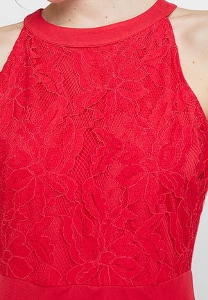 Primer plano de vestido rojo sin mangas con encaje floral superpuesto y escote alto en la parte superior del torso de una persona.