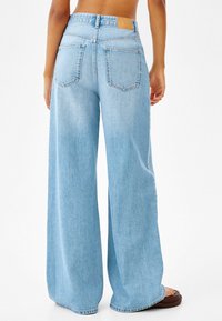 Ljusblå denimbyxor med vida ben och hög midja, två bakfickor och en läderlapp på midjebandet. Slät textur, avslappnad passform.