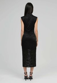 Robe midi en dentelle noire avec des manches courtes, présentant une silhouette ajustée et un motif floral. Le tissu transparent permet de voir la peau en dessous.