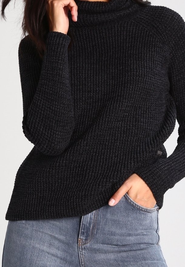 Suéter negro de cuello alto de punto acanalado con mangas largas, que presenta un corte holgado y una superficie texturizada, combinado con jeans azul claro.
