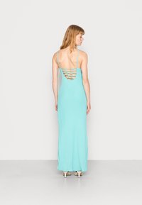 Vestido maxi em tecido azul claro, com silhueta ajustada e design recortado nas costas com alças horizontais. Alças finas e textura suave.