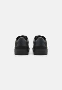 Sneakers neri con pannelli grigi testurizzati, suole in gomma piane e design minimalista. Presentano un retro arrotondato e accenti di branding discreti.