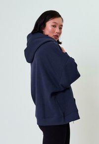Hoodie oversized color navy, realizzato in tessuto morbido, con un ampio cappuccio, spalle scese, polsini a costine e tasca a marsupio.