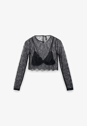 Top court en dentelle noire à manches longues, avec un voile transparent et un soutien-gorge noir uni en dessous. Tissu délicat et texturé.
