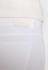 Bílé džíny z denimu s hladkou strukturou, zdobené koženou nášivkou s logem, s pětipoklopovým střihem a jemnými švy.