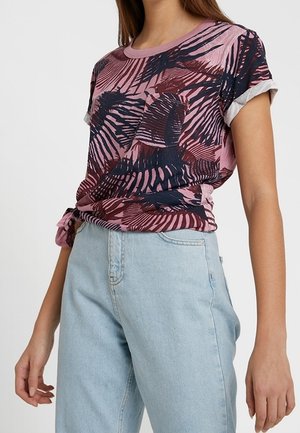 Mujer vistiendo una camiseta de manga corta con estampado abstracto en rosa y azul marino con puños enrollados y pantalones vaqueros de tiro alto en azul claro.