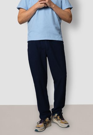 Hellblaues Kurzarmhemd mit strukturierter Oberfläche, kombiniert mit locker sitzender, marineblauer Hose und beige Sneakern mit schwarzen und blauen Akzenten.