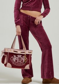 Felpa bordeaux in velluto con giacca cropped a zip e pantaloni a zampa, abbinata a una borsa a tracolla Juicy Couture bordeaux e rosa con dettagli dorati.