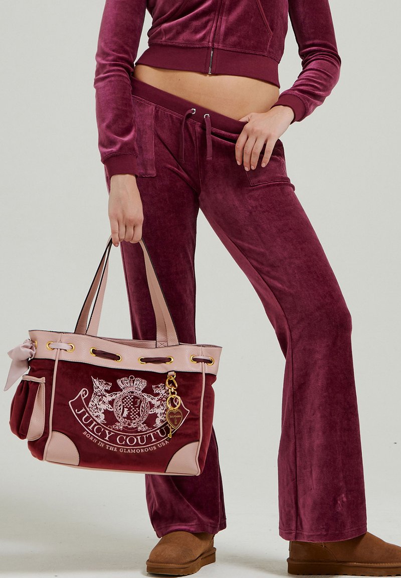 Felpa bordeaux in velluto con giacca cropped a zip e pantaloni a zampa, abbinata a una borsa a tracolla Juicy Couture bordeaux e rosa con dettagli dorati.