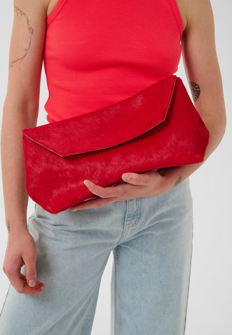 Red rectangular clutch bag made of textured fur-like material, features a large flap closure and smooth edges, held under the arm.