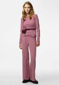 Rotes und weiß gestreiftes Langarm-Top kombiniert mit passenden, weiten Hosen. Mit einem burgunderroten Gürtel mit kleinem Täschchen gebunden. Schwarze Schuhe.