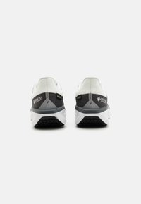 Zapatos de senderismo blancos y grises con una parte superior texturizada, etiquetado de Gore-Tex y suela de goma negra con patrón, diseñados para durabilidad y comodidad.
