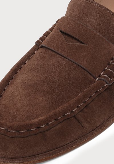 Mocassin en daim marron avec couture style mocassin et une petite découpe décorative sur la partie supérieure de la chaussure.