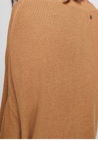 Sweter w kolorze camel z dzianiny, z teksturowanym wzorem i okrągłym dekoltem. Z tyłu widoczny jest mały detal z logo.