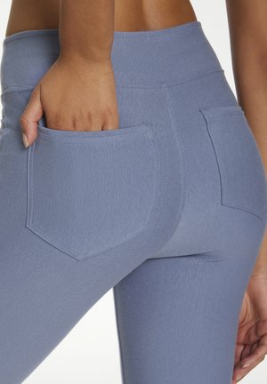 Hochgeschnittene blaue Leggings aus strukturiertem Stoff, mit sichtbaren Gesäßtaschen und einer eng anliegenden Passform an Hüften und Oberschenkeln.