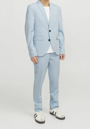 Hellblauer Anzug mit zwei Knöpfen, Stegkragen und Seitentaschen; kombiniert mit einem weißen T-Shirt und mehrfarbigen Sneakers.