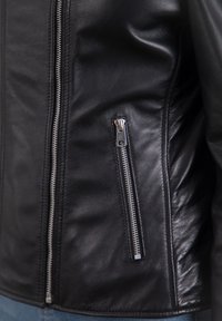 Black leather jacket featuring a fitted design with a prominent silver zipper pocket and smooth texture, showcasing a sleek, contemporary silhouette.