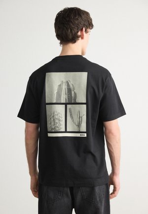 T-shirt in cotone nero con una stampa grafica di cactus disposti a griglia sul retro. Maniche corte, collo tondo, vestibilità rilassata.