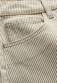 Close-up van beige en bruin gestreepte denimstof met een gestikte voorzak en riemlusdetail.