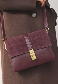 Burgundy handbag made of leather and suede, featuring a textured flap with embossed crocodile pattern and a gold-tone latch closure.