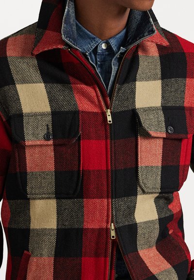 Red, black, and beige plaid jacket with a zip front, two chest pockets, and a collared design. Fabric appears textured and warm.