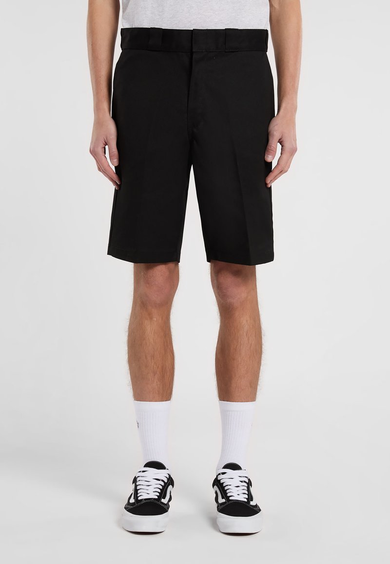 Black shorts with a straight cut, featuring a belt, smooth fabric texture, and pockets. Worn with black sneakers and white socks.