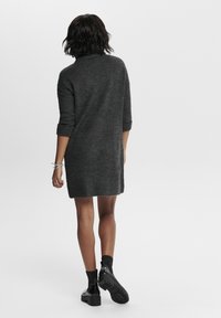 Robe pull gris charbon avec un col montant, des manches trois-quarts et une coupe décontractée, associée à des bottines et des chaussettes noires.