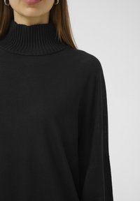 Črn pulover s turtleneck ovratnikom, rebrasto teksturo, mehak material, ohlapen kroj in spuščena ramena, osredotočen na eleganten, minimalističen dizajn.