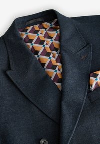 Marinblå blazer med en texturerad finish, utrustad med ett mönstrat foder i orange, vinröd och svart, samt en matchande näsduk.