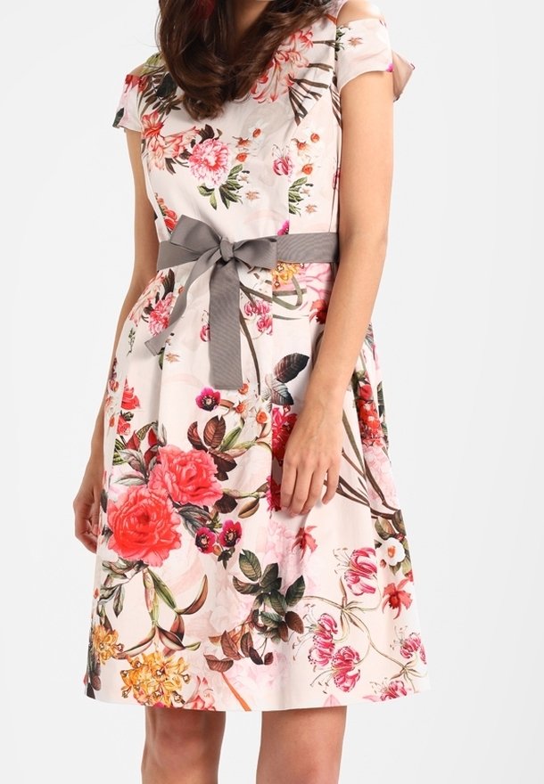 Donna che indossa un vestito fino al ginocchio, a maniche corte, con stampa floreale colorata e un nastro grigio in vita annodato a fiocco.