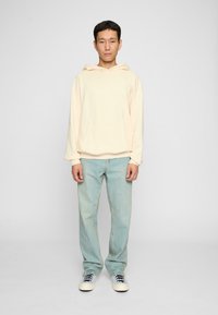 Light yellow hoodie with a front pocket, paired with light blue, straight-leg jeans and white sneakers with black laces. Simple design.