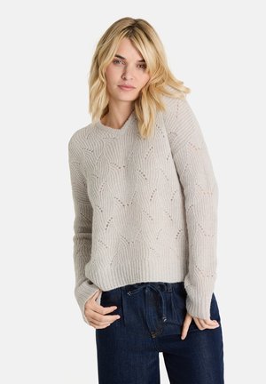 Hellgrauer Strickpullover mit einem strukturierten Wellenmuster, gerippten Bündchen und Saum sowie einem lässigen Schnitt. Getragen mit dunkelblauen Jeans.