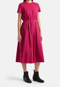 Fuksia puuvillane kleit lühikeste varrukatega, vöökoht on rõhutatult kitsas ja seelikuosa voolab. Kombineeritud mustade pahkluu saapatega, millel on sangade detail.