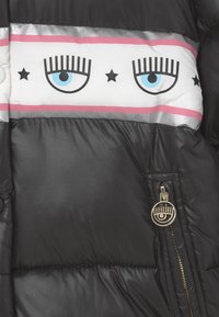 Černá péřová bunda s bílým páskem zdobeným modrýma očima a hvězdami, kovovými doplňky a zlatým jezdcem zipu s grafikou oka.