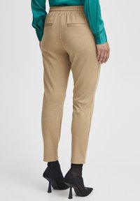 Beige joggers med elastisk midja, två bakfickor, smal passform och mjuk textur. Matchas med genomskinliga svarta högklackade stövlar.