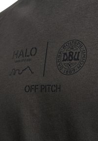 Dunkelgrauer Stoff mit glatter Textur zeigt schwarze Drucklogos: "HALO", "OFF PITCH" und das Emblem der Dansk Boldspil Union.