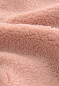 Puha, strukturált fleece anyag világos rózsaszín színben, vastag, bolyhos felülettel, szabálytalan mintázattal és meleg, kényelmes megjelenéssel.