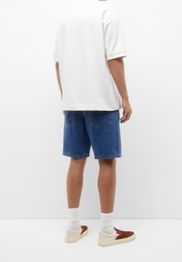Camiseta de algodón blanca, corte relajado, manga corta. Pantalones cortos de mezclilla azules, hasta la rodilla. Calcetines blancos hasta el tobillo y zapatos marrones de slip-on.