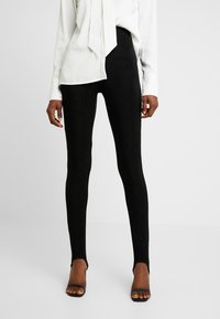 Svarta ribbade leggings med en texturerad yta, med hög midja och bärs med öppna svarta skor.