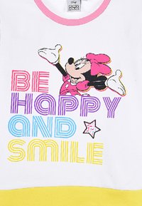 Witte katoen t-shirt met kleurrijke tekst "WEES GELUKKIG EN GLIMLACH" met gele, blauwe, paarse en roze accenten; illustratie van een cartoonpersonage.