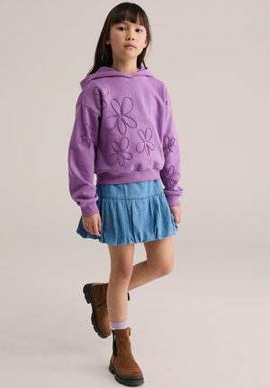 Purpurinis medvilninis džemperis su siuvinėtomis gėlių raštais, derinamas su mėlyna džinsine suknele ir rudu kulkšnių ilgio batais.