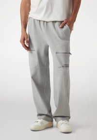 Light gray sweatpants made of soft fabric, featuring zippered pockets, a relaxed fit, and contrasting stitching details.