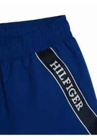 Pantaloni sportivi blu navy con vita elasticizzata, caratterizzati da una striscia laterale nera con il testo bianco "HILFIGER". Tessuto morbido con una superficie leggermente lucida.