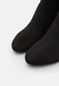 Bottines en suède noir avec une texture lisse, un design à bout pointu et des panneaux latéraux élastiques. La semelle est légèrement courbée pour un confort accru.