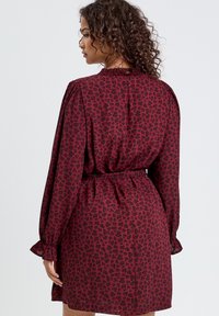 Czerwona sukienka z lekkiego materiału w czarne serca, z długimi rękawami, ściągniętą talią i falbanami przy mankietach.