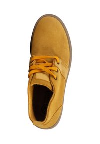 Chaussure en daim jaune avec semelle en caoutchouc marron, dotée de lacets jaunes et d'un bout arrondi. L'intérieur présente une doublure douce et des détails de logo.