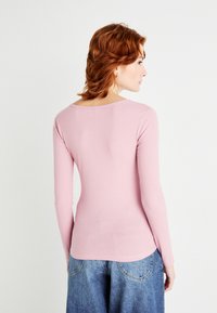 Langermet, ribbestrikket rosa topp med rund halslinning, tettsittende fasong og myk tekstur, sammen med løse, lyseblå denimbukser.