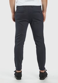Marineblaue Slim-Fit-Hosen mit strukturiertem Finish, ausgestattet mit zwei Gesäßtaschen und Knöchelbündchen, kombiniert mit schwarzen Schuhen.