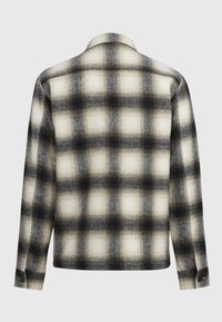 Camisa de manga larga con un patrón a cuadros difuminado en negro, gris y blanco, con puños abotonados, mostrada desde la parte posterior sobre un fondo liso.