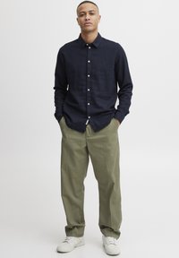 Camisa de manga larga color navy con botones, pantalones de pierna ancha color verde oliva y zapatillas blancas. La tela parece ligera con una textura suave.